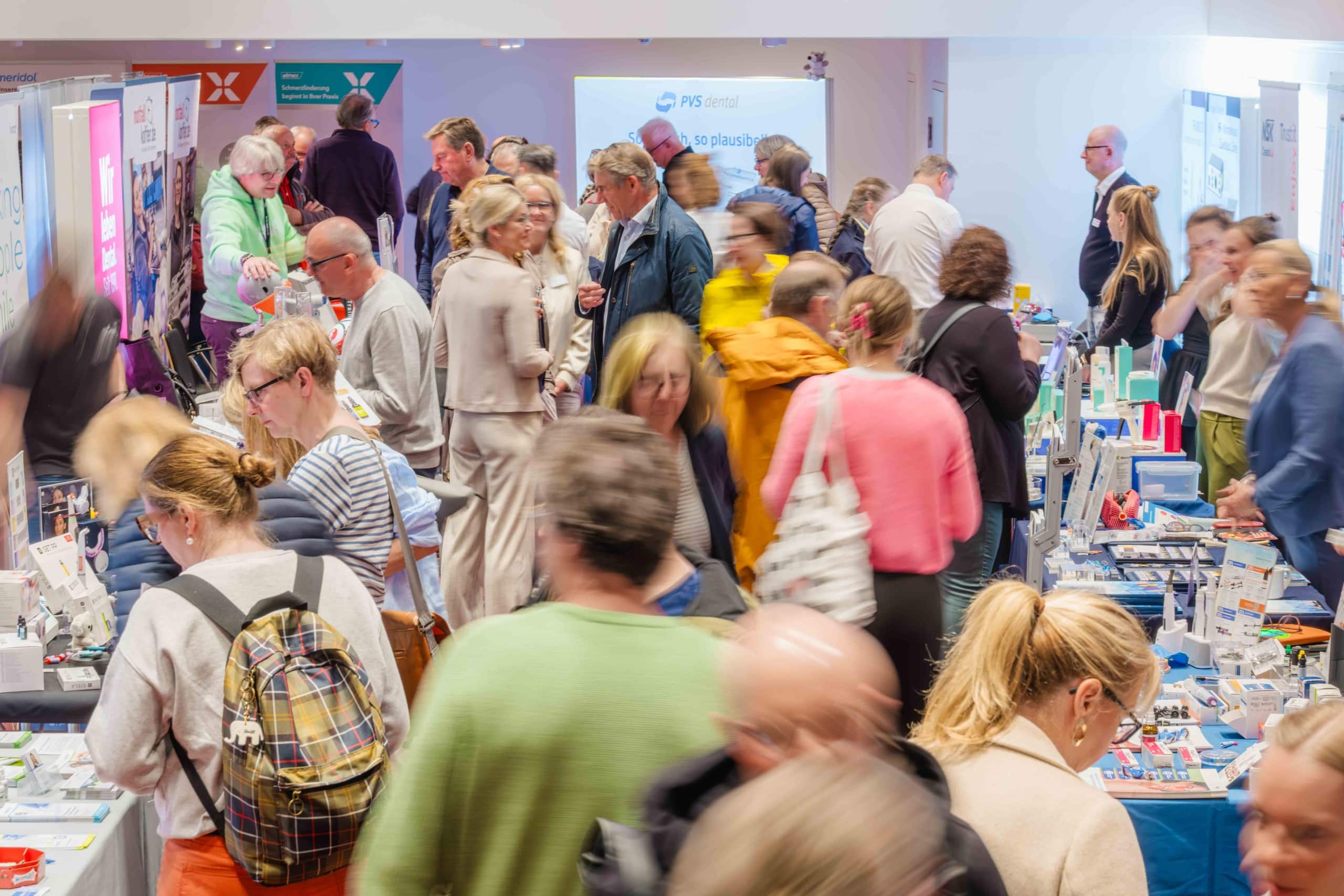 Eine gut besuchte Messe in den Innenräumen, auf der viele Menschen umhergehen und an verschiedenen Ständen stöbern, an denen Produkte und Informationsmaterialien auf Tischen ausgestellt sind. Die Atmosphäre ist lebhaft und es herrscht reges Treiben, während sich die Besucher angeregt unterhalten.
